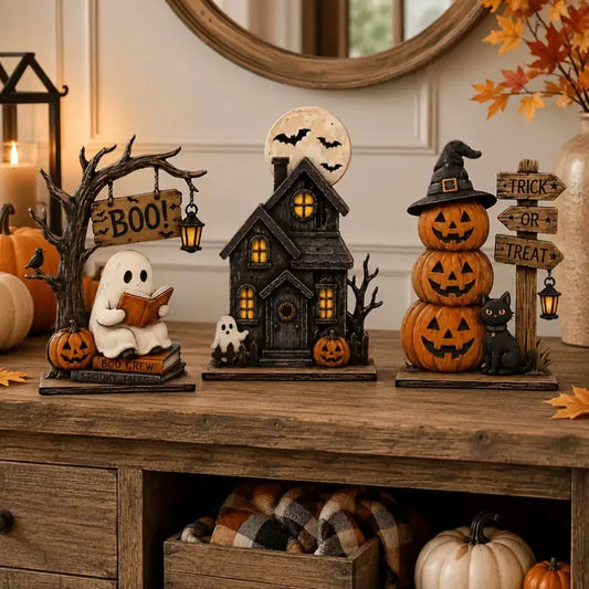 Close-up of The Boo Crew Halloween tabletop set - haunted house, ghost reading a book, and jack-o'-lantern witch with black cat - styled on a wood counter.